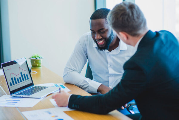 Dois homens fazendo o planejamento de marketing conversacional na mesa do escritório com o notebook e papéis.