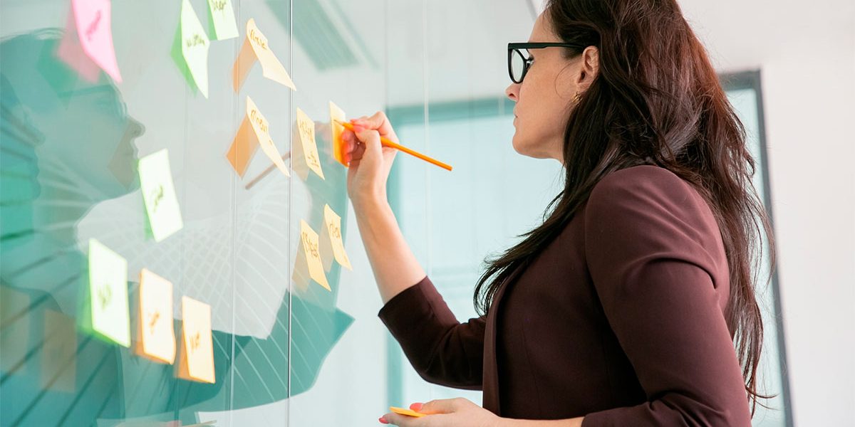 Metas-de-Marketing-2023 Mulher anotando em post-its as metas de marketing 2023 de sua empresa.