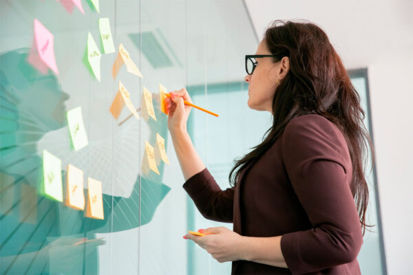 Mulher anotando em post-its as metas de marketing 2023 de sua empresa.